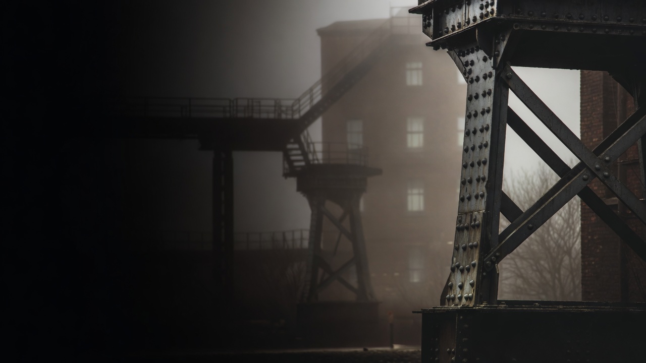 Riveted rusted steel beams in fog, a brick factory and gantry beyond
