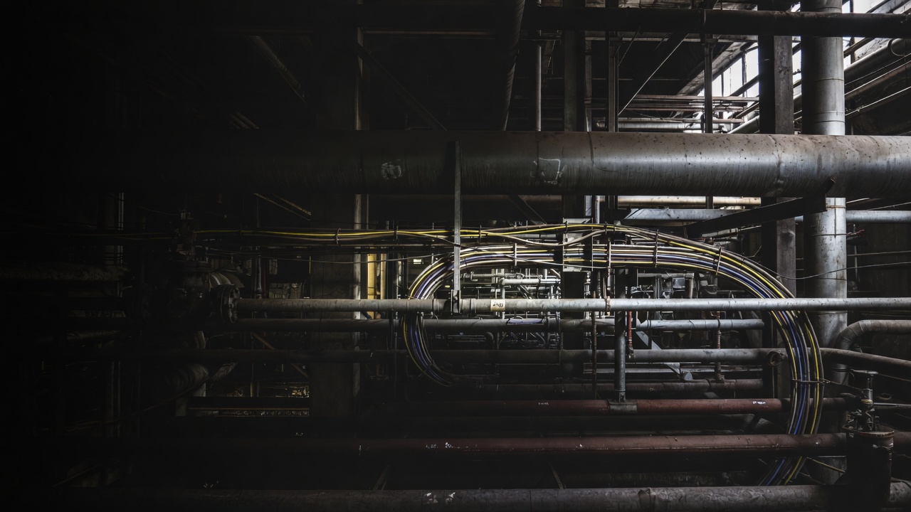 Dark steel pipes and yellow-and-blue cable bundles in an industrial plant