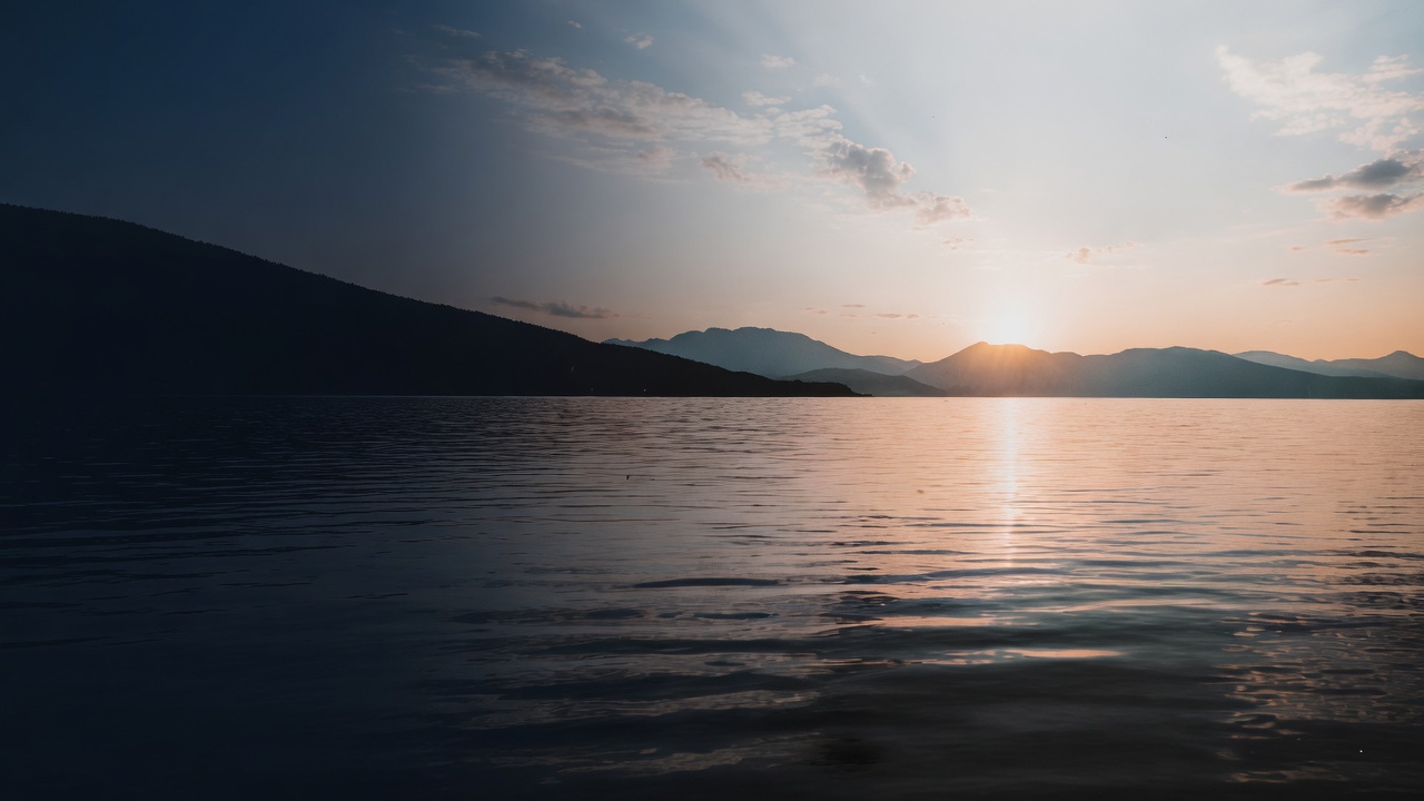 A still lake at sunrise with a path of light and distant mountains