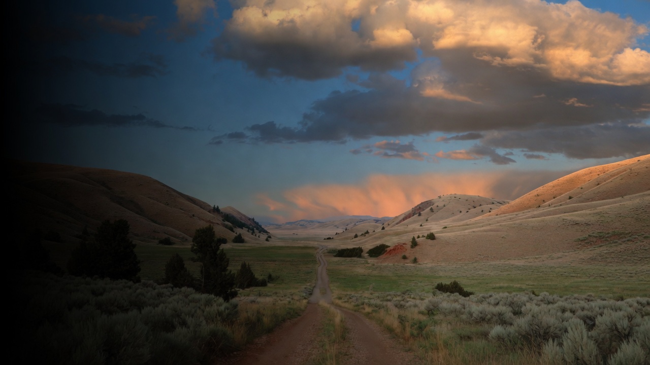 A two-track dirt road runs through sage hills under peach-and-blue clouds
