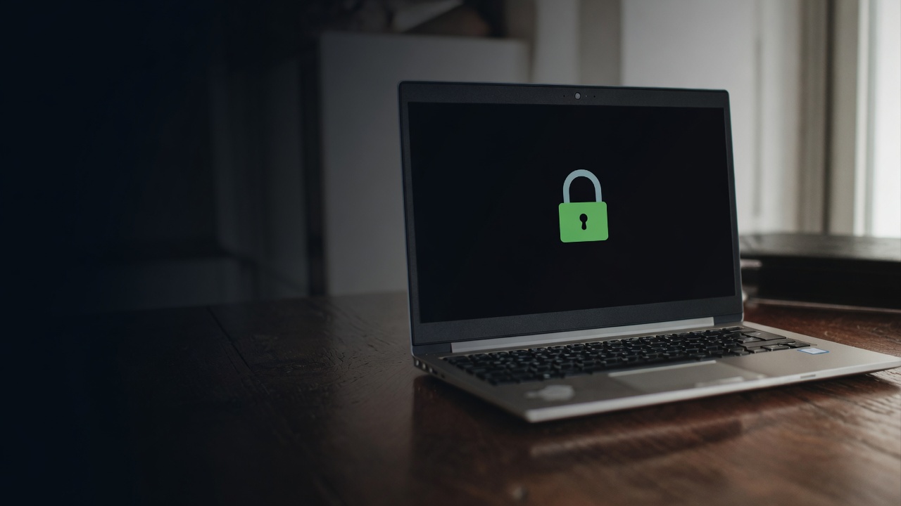 A silver laptop on a dark wood table shows a simple green padlock